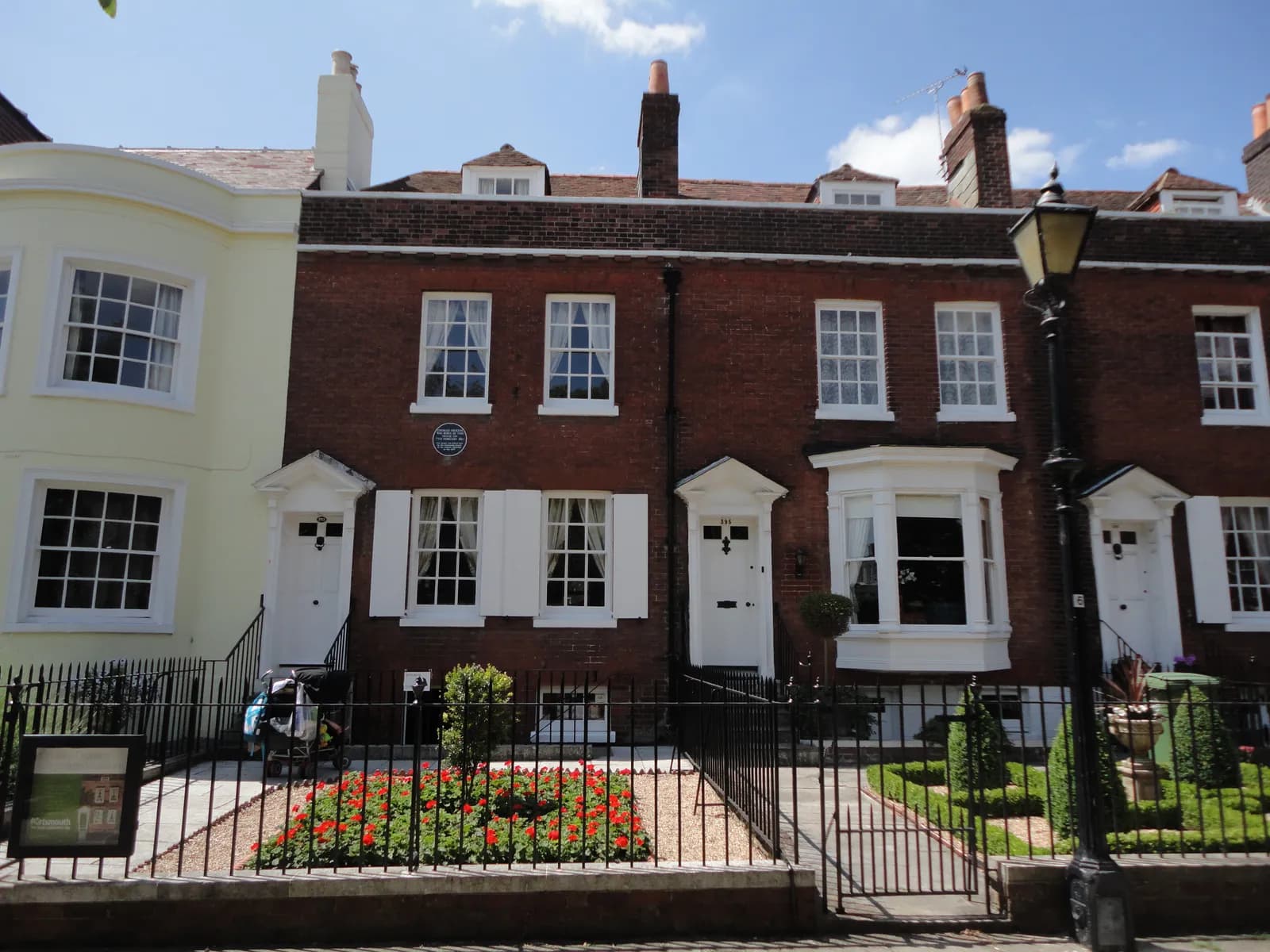 A row of historic brick houses with white windows and doors, some with small front gardens, under a clear blue sky.